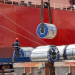 Packaged coils, galvanized steel and large tin rolls are loaded onto the ship by crane from heavy duty trucks for shipment.